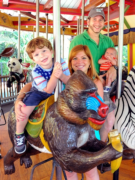 Family enjoying carousel ride at Zoo Miami with animal figures.