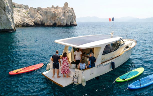 Boat tour at Frioul Archipelago with passengers boarding near rocky coastline.