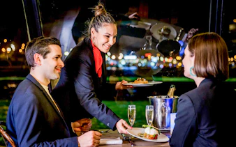 Waiter serving dinner to couple on Seine River cruise in Paris.