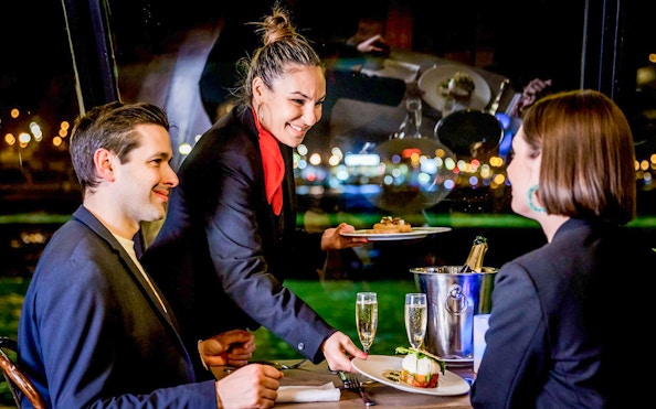 Waiter serving dinner to couple on Seine River cruise in Paris.
