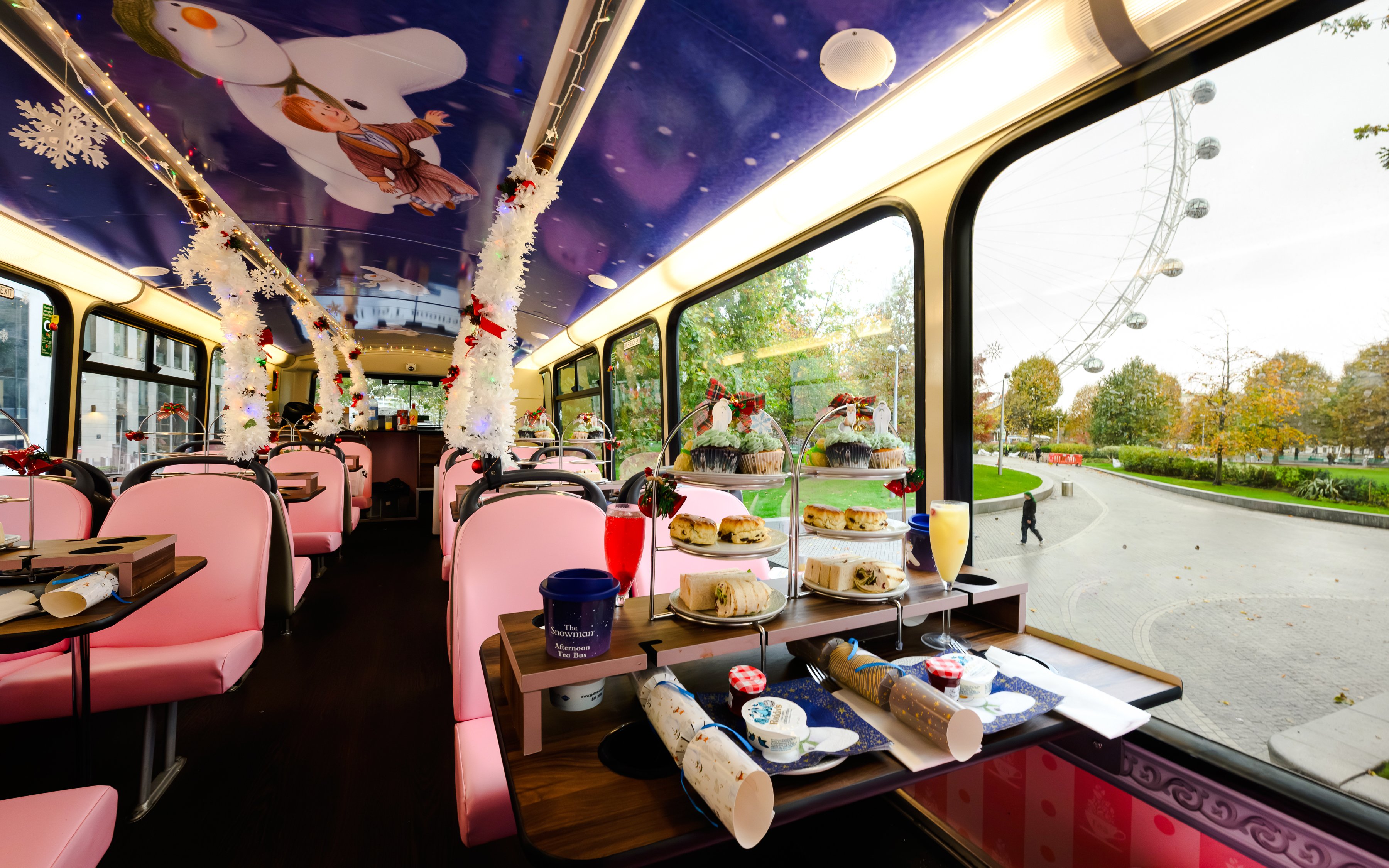 Afternoon tea setup inside a decorated bus with The Snowman™ theme, overlooking the London Eye.