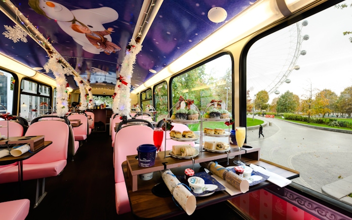 Afternoon tea setup inside a decorated bus with The Snowman™ theme, overlooking the London Eye.