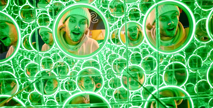 Man's face reflected in multiple green-lit mirrors at World of Illusions, Dublin.