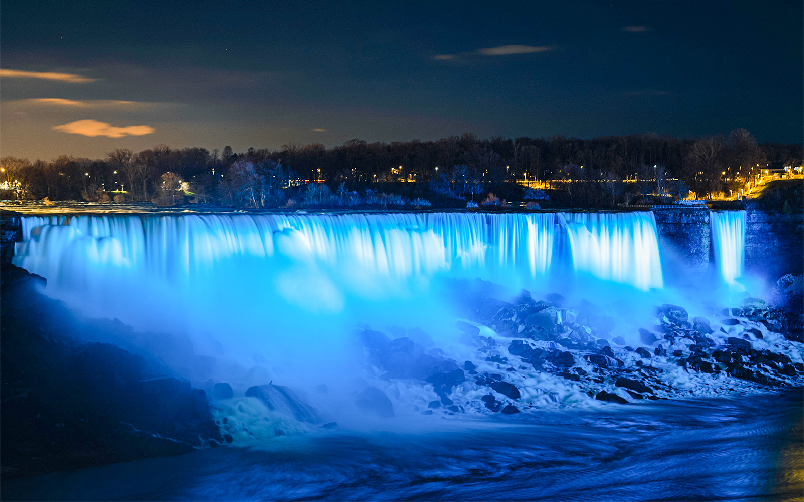 Niagara Falls illuminated in blue during night light show.