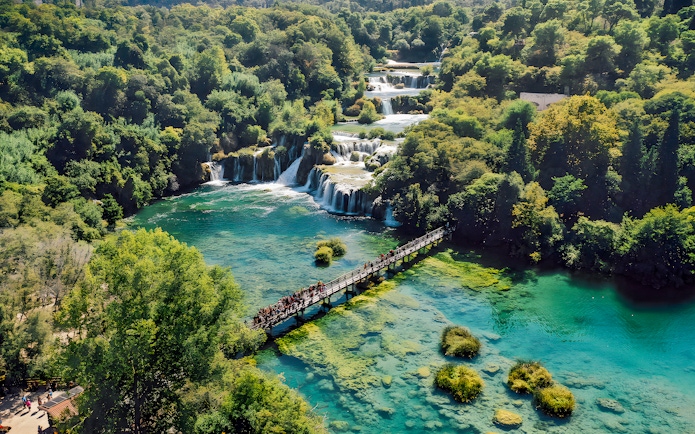 Visitors walking on a bridge over turquoise water at Krka National Park, Croatia.