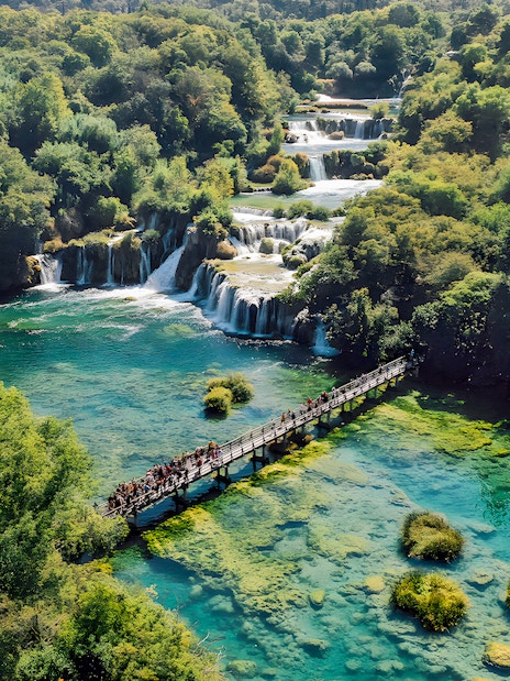 Visitors walking on a bridge over turquoise water at Krka National Park, Croatia.