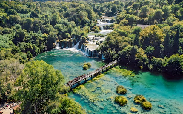 Visitors walking on a bridge over turquoise water at Krka National Park, Croatia.
