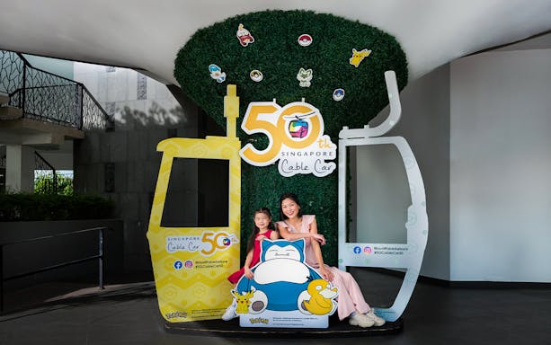 Family posing at Singapore Cable Car 50th Anniversary display with cartoon characters.