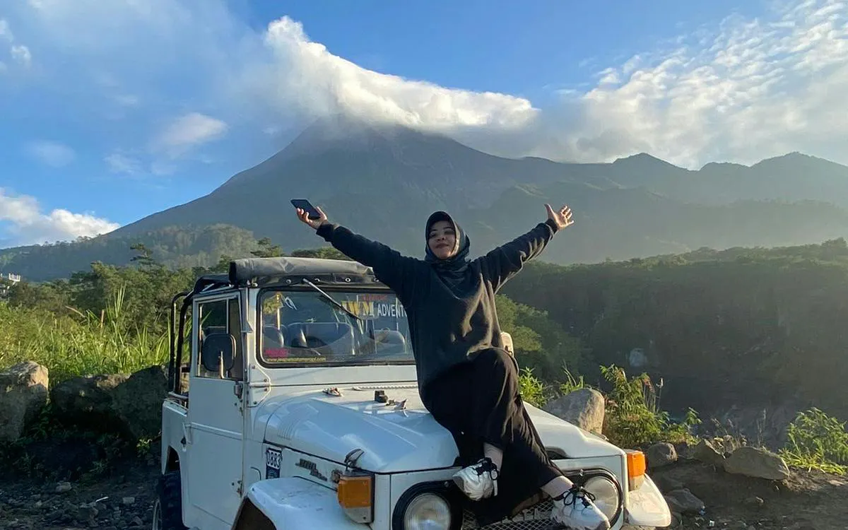 Person sitting on a jeep with arms outstretched, Mount Merapi in the background, Sunrise Long Trip Lava Tour, Dubai.