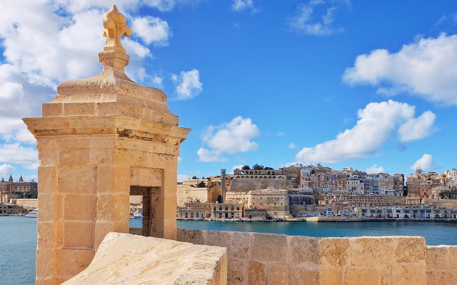 Fortified city view with stone watchtower and harbor, Malta.