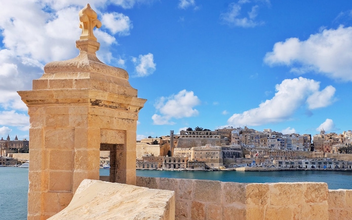 Fortified city view with stone watchtower and harbor, Malta.