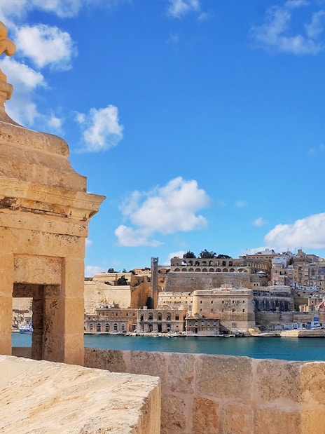 Fortified city view with stone watchtower and harbor, Malta.