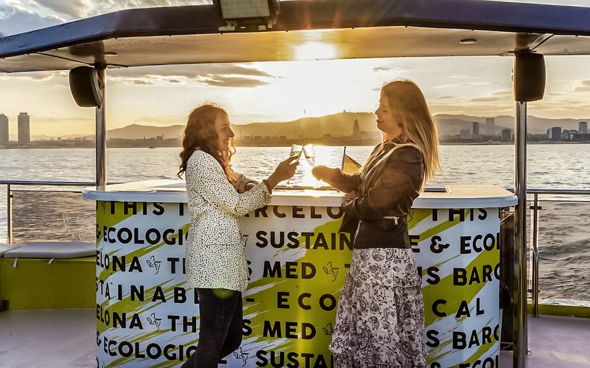 Two people enjoying drinks on a catamaran cruise in Barcelona at sunset.