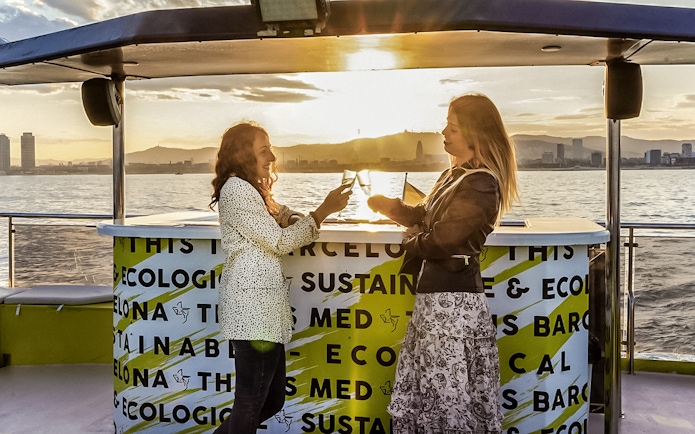 Two people enjoying drinks on a catamaran cruise in Barcelona at sunset.