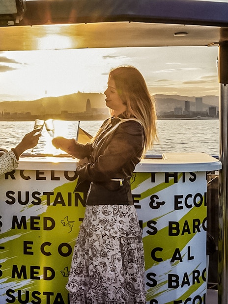 Two people enjoying drinks on a catamaran cruise in Barcelona at sunset.
