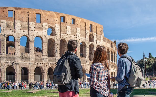 Tourists with backpacks viewing the Colosseum in Rome.