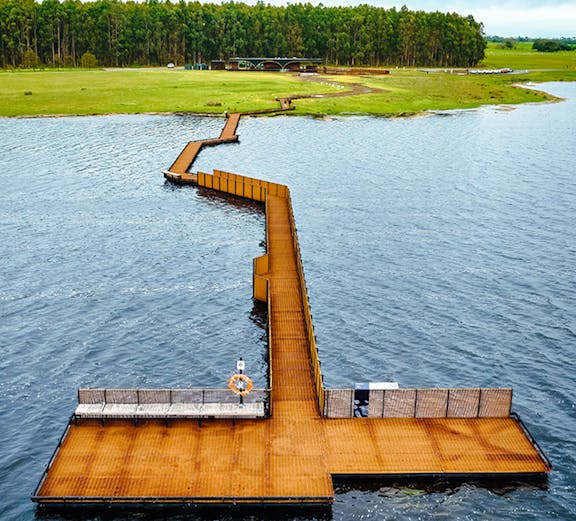 Floating walkway over water at Budj Bim Cultural Landscape, surrounded by greenery and trees.