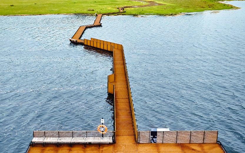 Floating walkway over water at Budj Bim Cultural Landscape, surrounded by greenery and trees.