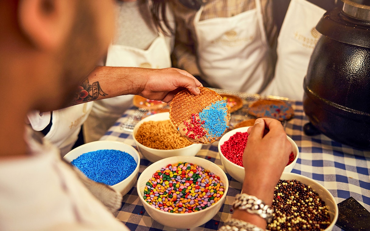 Dutch syrup waffle being decorated with colorful sprinkles at a workshop.