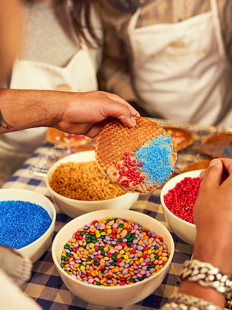 Dutch syrup waffle being decorated with colorful sprinkles at a workshop.