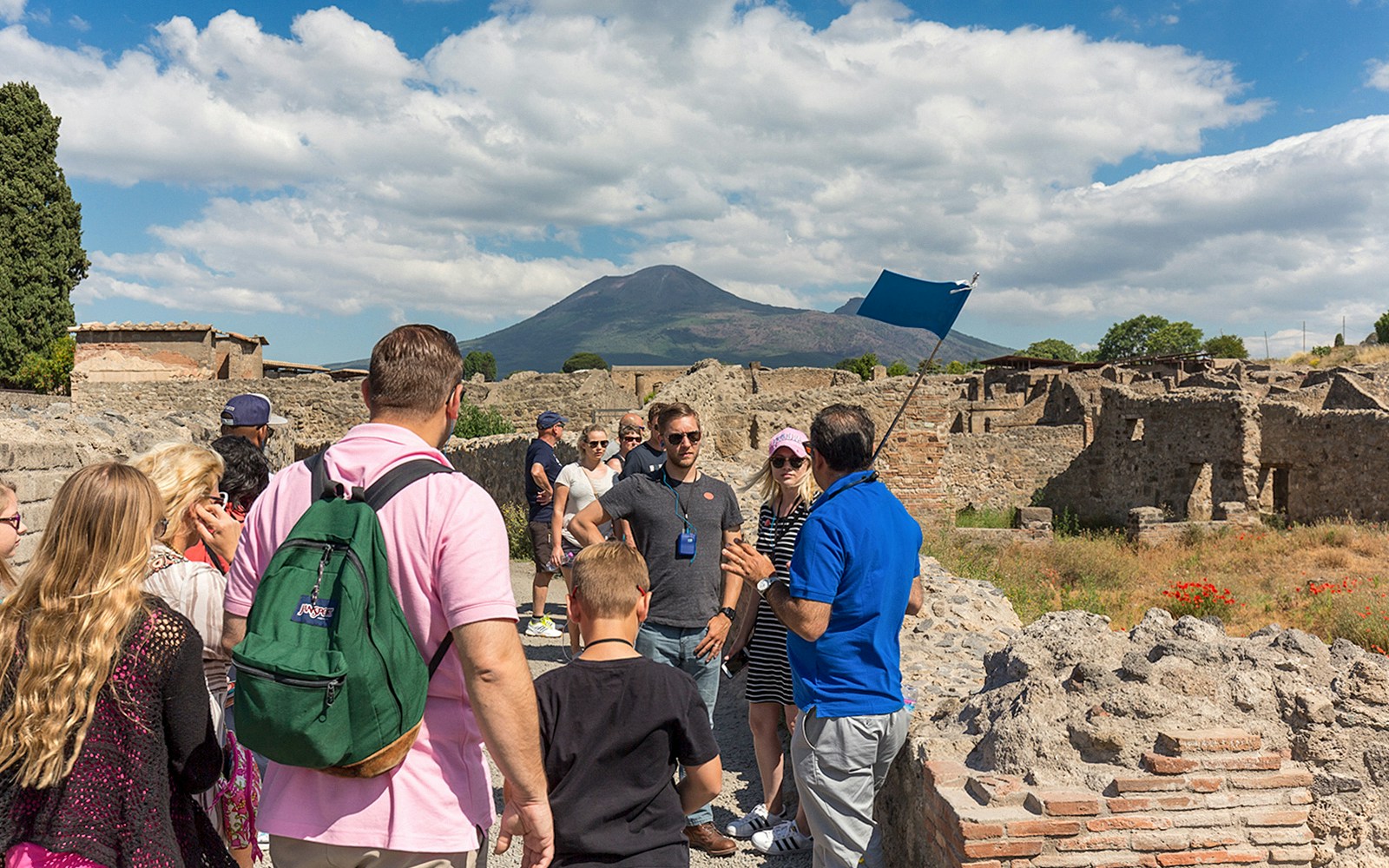 Guide explaining Pompeii ruins to tourists with Mount Vesuvius in the background.