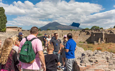 Guide explaining Pompeii ruins to tourists with Mount Vesuvius in the background.