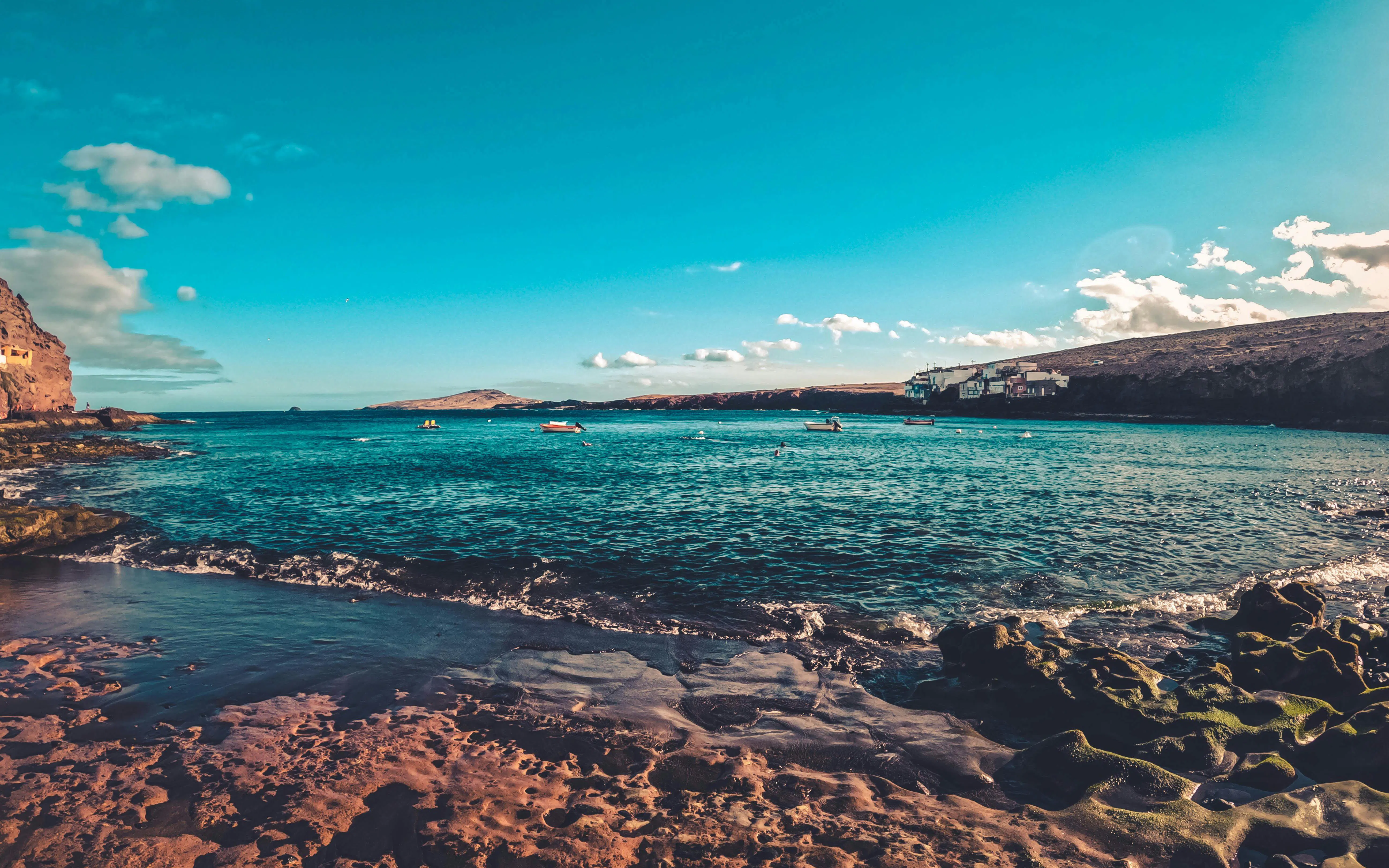 Coastal view of Red Canyon, Gran Canaria, with rocky shoreline and distant boats.