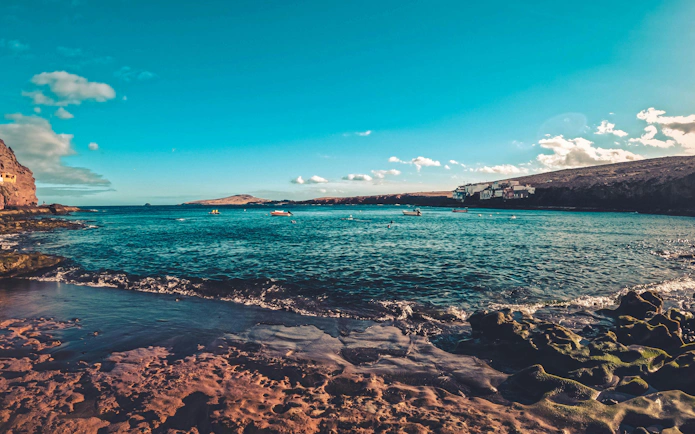 Coastal view of Red Canyon, Gran Canaria, with rocky shoreline and distant boats.