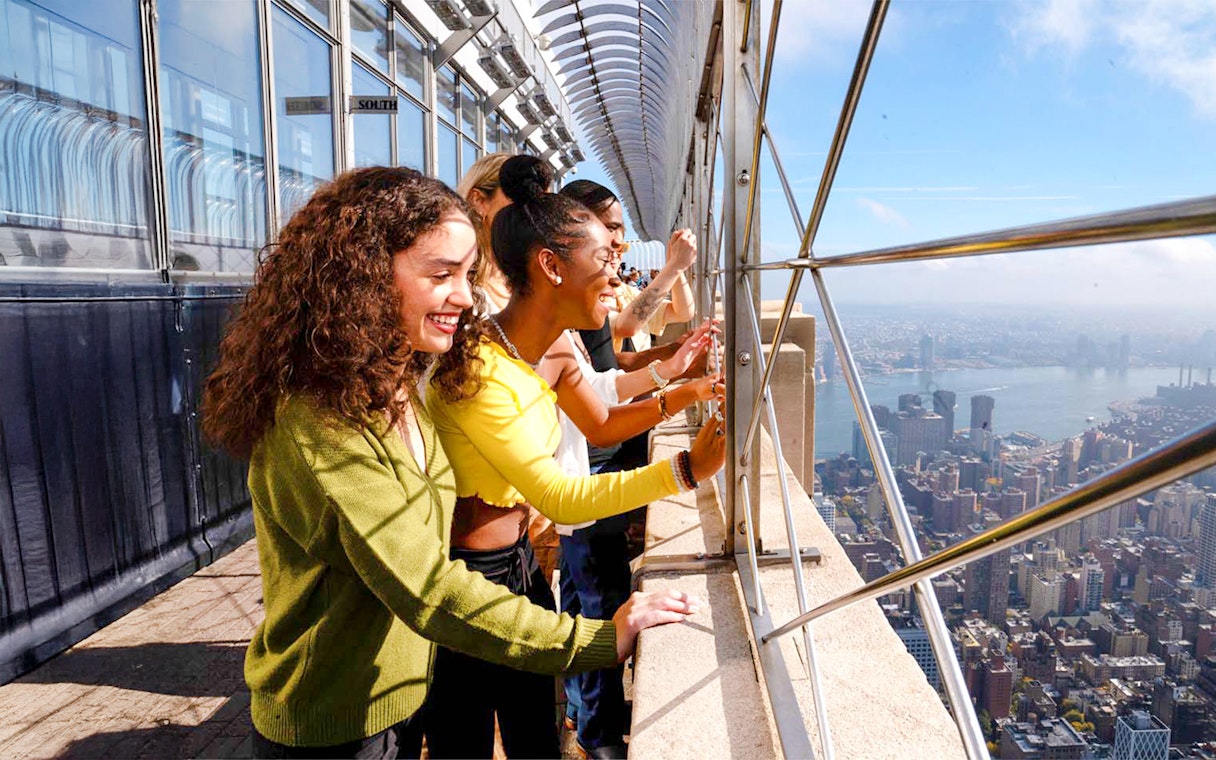 Tourists viewing New York City skyline from Empire State Building observation deck.