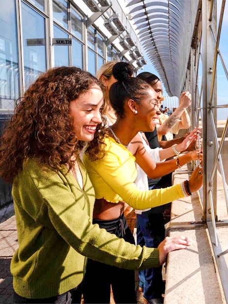 Tourists viewing New York City skyline from Empire State Building observation deck.