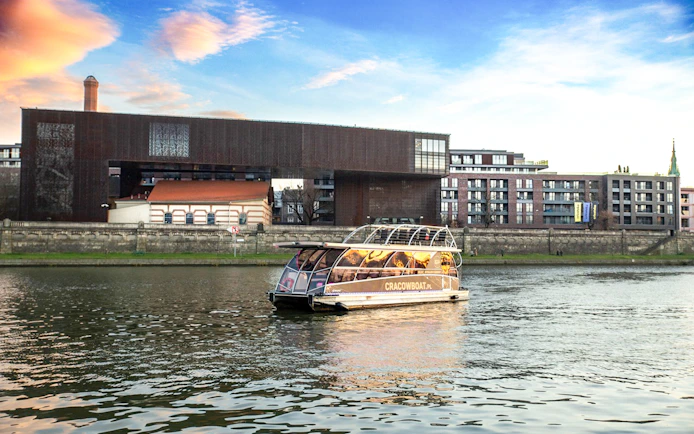 Catamaran cruising on the Vistula River in Krakow with modern buildings in the background.