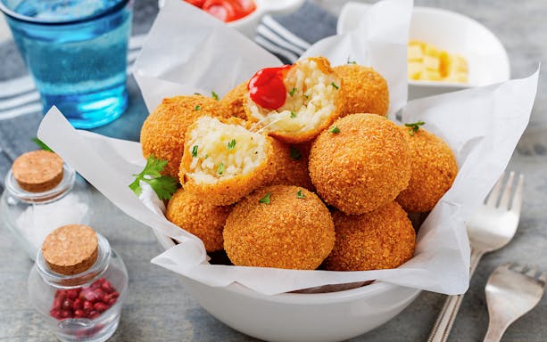 Risotto balls with crispy coating in a bowl, garnished with herbs.