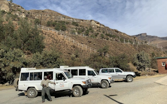 Off-road vehicles parked at Sani Pass with a guide, showcasing rugged mountain terrain near Durban.