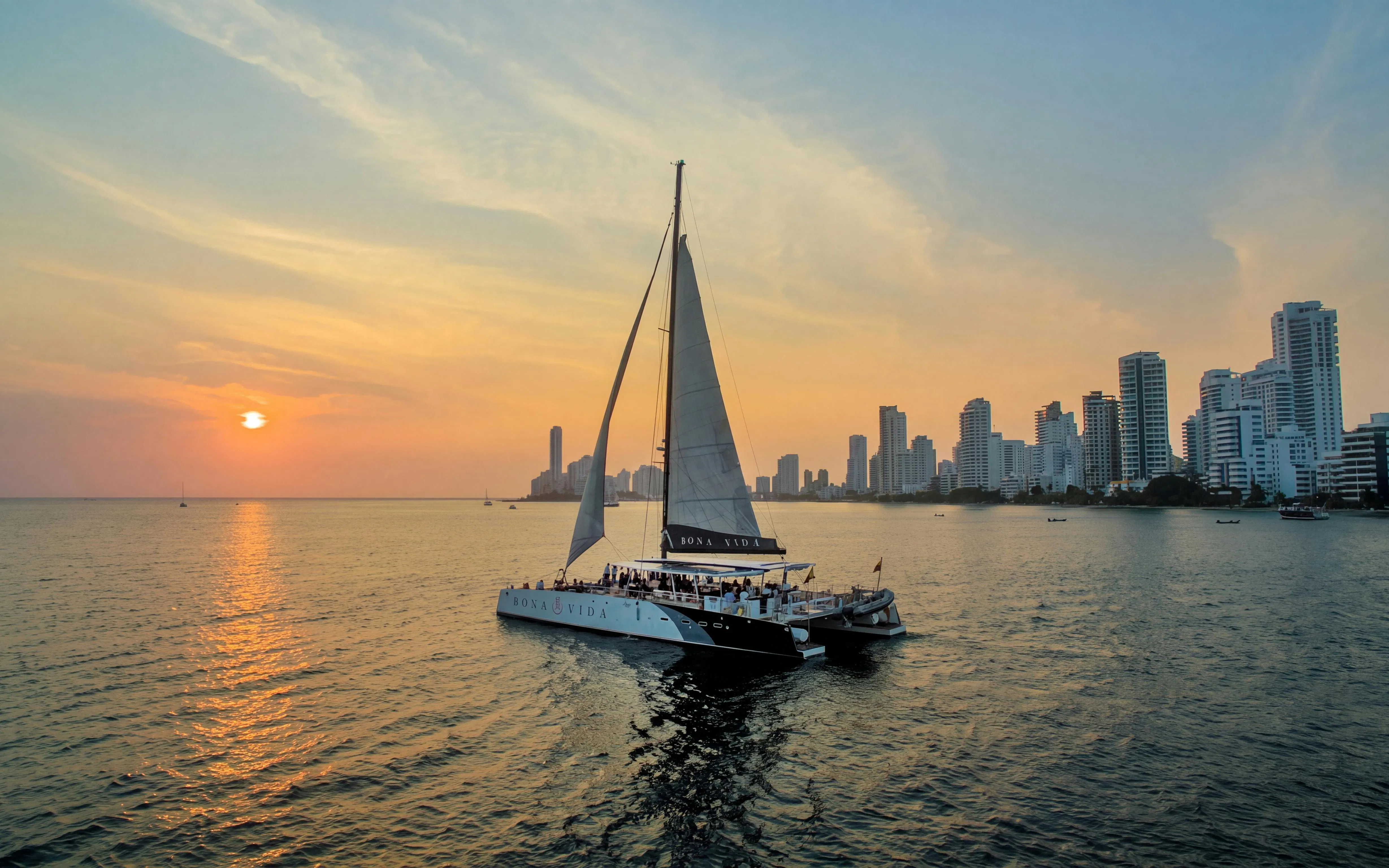 Catamaran sailing at sunset near Cartagena skyline.