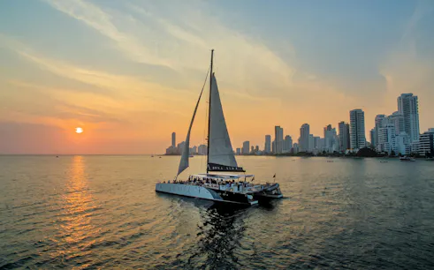 Catamaran sailing at sunset near Cartagena skyline.