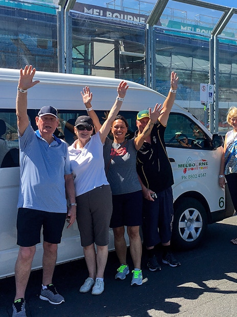 Group waving near Melbourne sports tour van at MCG.