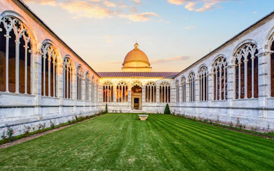 Pisa Monumental Complex courtyard with arches and dome at sunset, Italy.