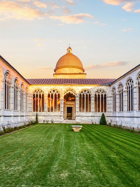 Pisa Monumental Complex courtyard with arches and dome at sunset, Italy.