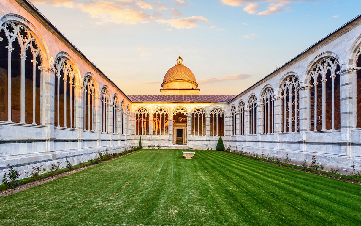 Pisa Monumental Complex courtyard with arches and dome at sunset, Italy.