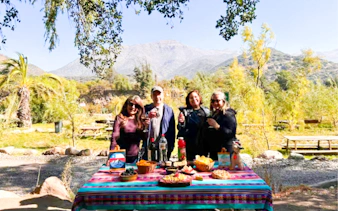 Group enjoying picnic with Chilean wine at Cajón del Maipo, Santiago, with mountains in the background.