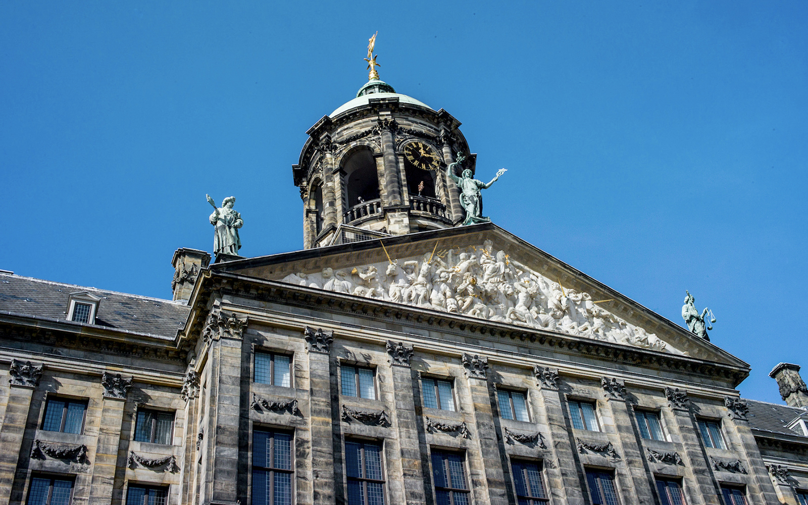Royal Palace of Amsterdam facade with sculptures and clock tower against blue sky.