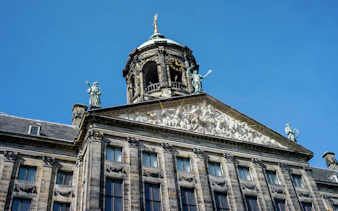 Royal Palace of Amsterdam facade with sculptures and clock tower against blue sky.