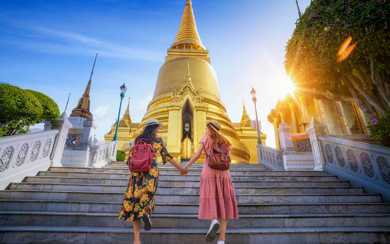 Two tourists ascending steps towards Bangkok's Grand Palace during a guided tour.