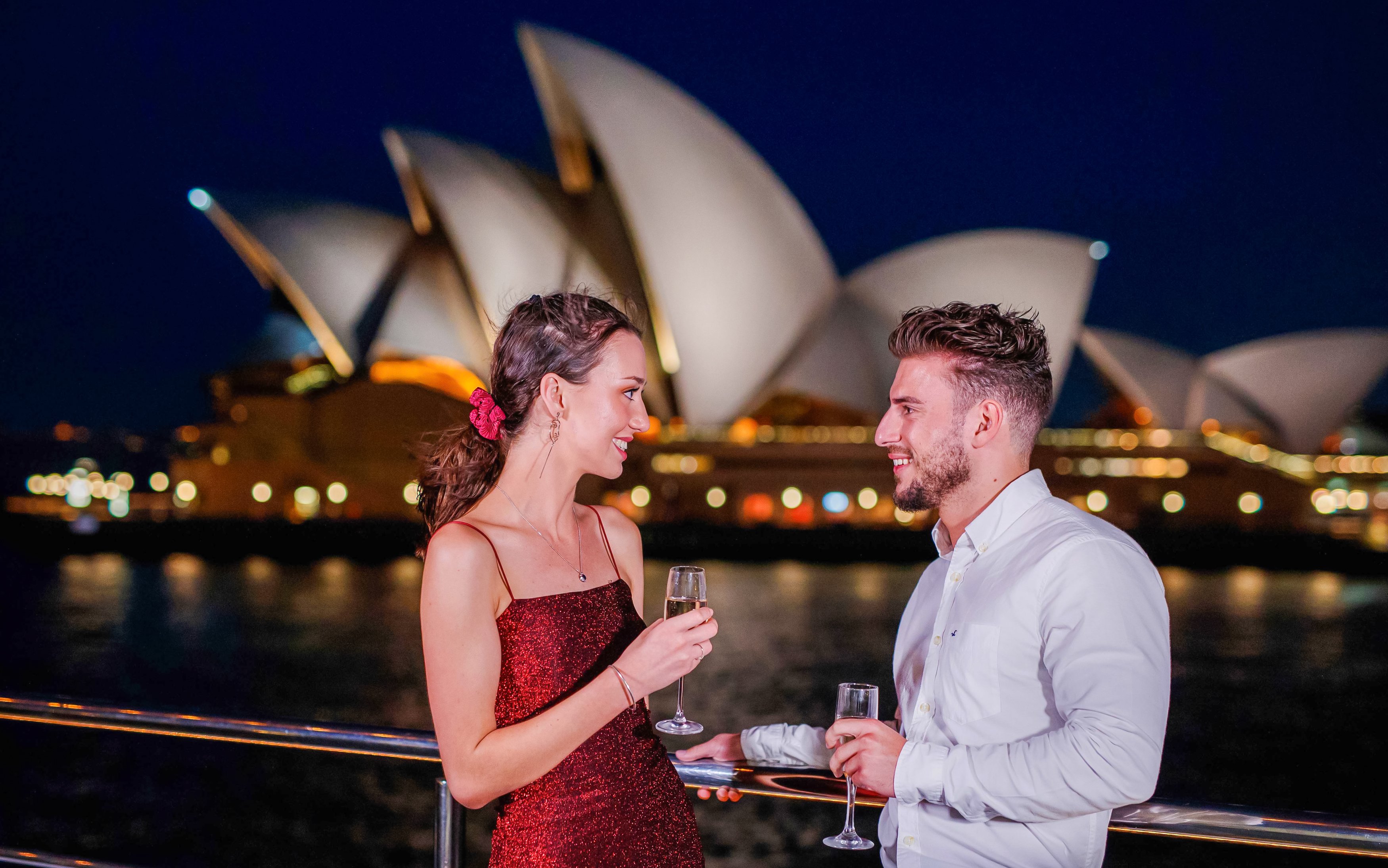 Couple enjoying drinks on a Sydney sunset cruise with Opera House in the background.