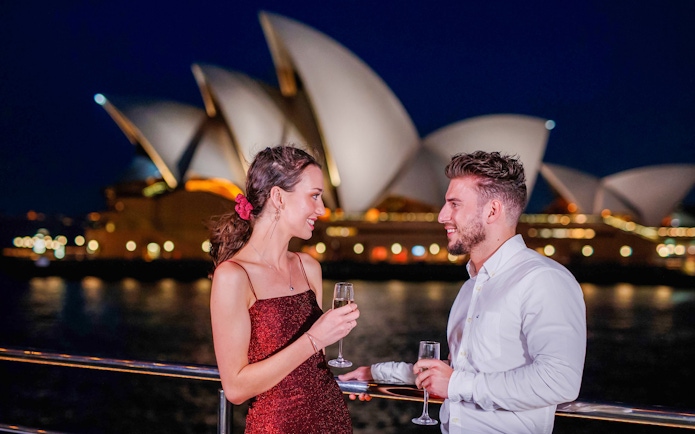 Couple enjoying drinks on a Sydney sunset cruise with Opera House in the background.