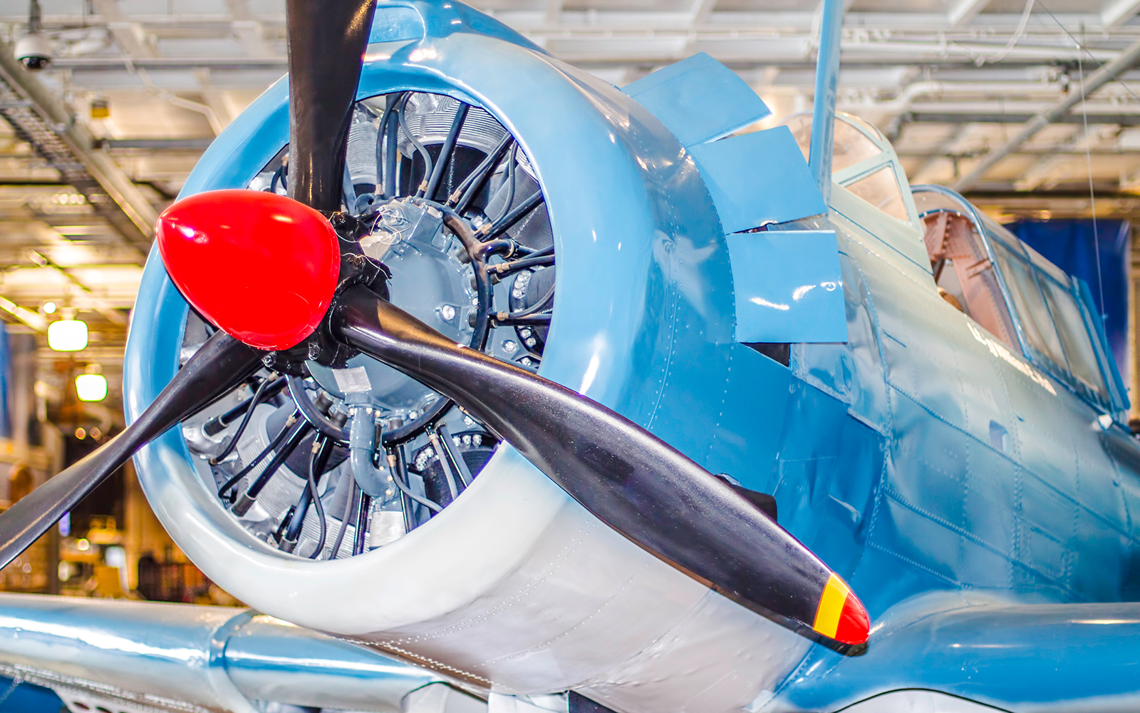 Front view of vintage blue airplane with red propeller in hangar.