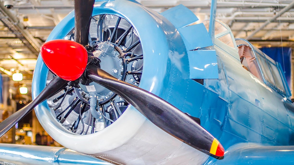 Front view of vintage blue airplane with red propeller in hangar.