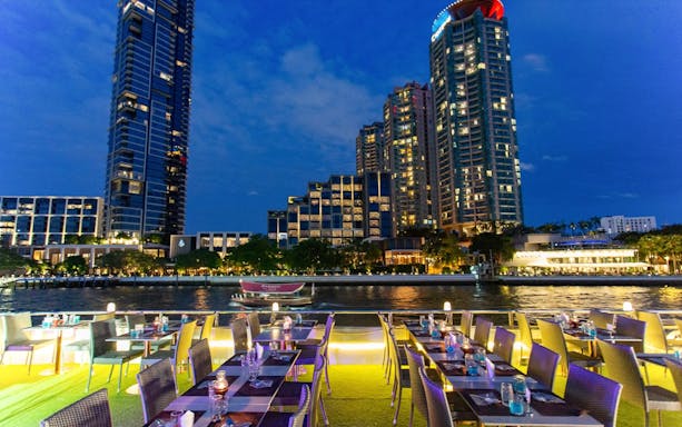 Dinner tables set on a cruise ship with city skyline view at IconSiam Pier No.4, Bangkok.
