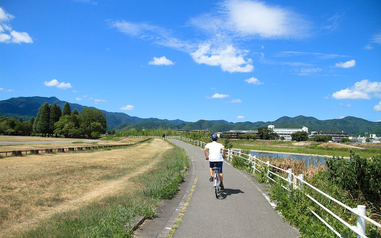 Cyclist on a scenic path along a river in Kyoto during a guided bike tour.
