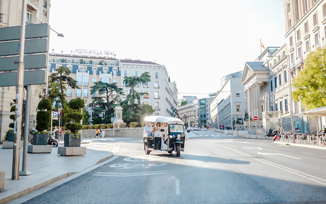 Electric tuk-tuk with tourists on a street near Hotel Villa Real, Madrid, Spain.